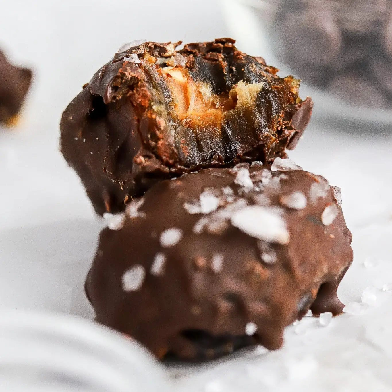 A chocolate-covered date with sea salt sprinkled on top, showing a visible spiced date-sweetened pecan filling.